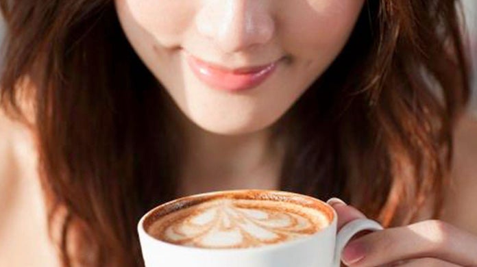 A lady smelling a cup of coffee