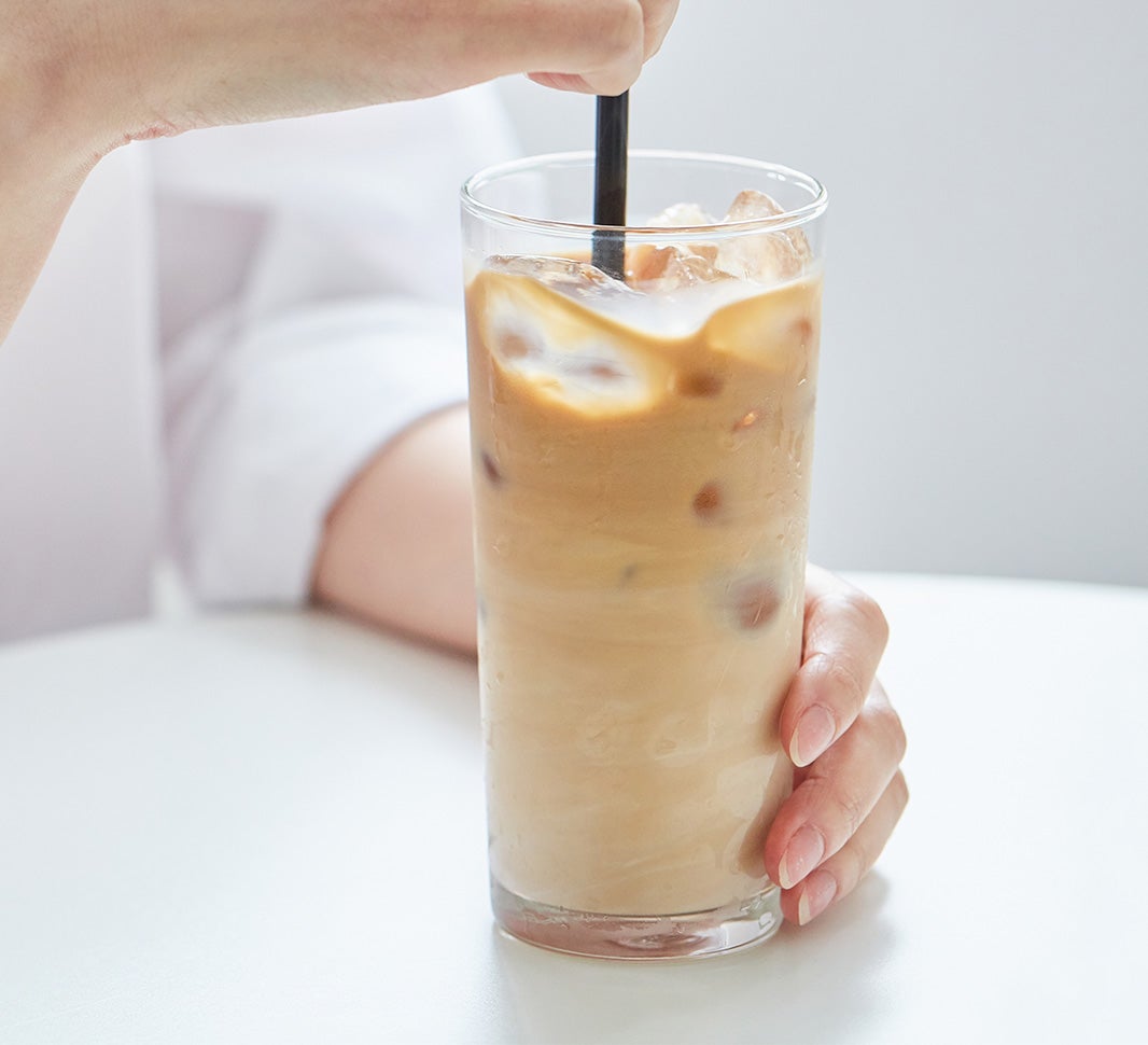 Stirring a glass of iced flat white coffee