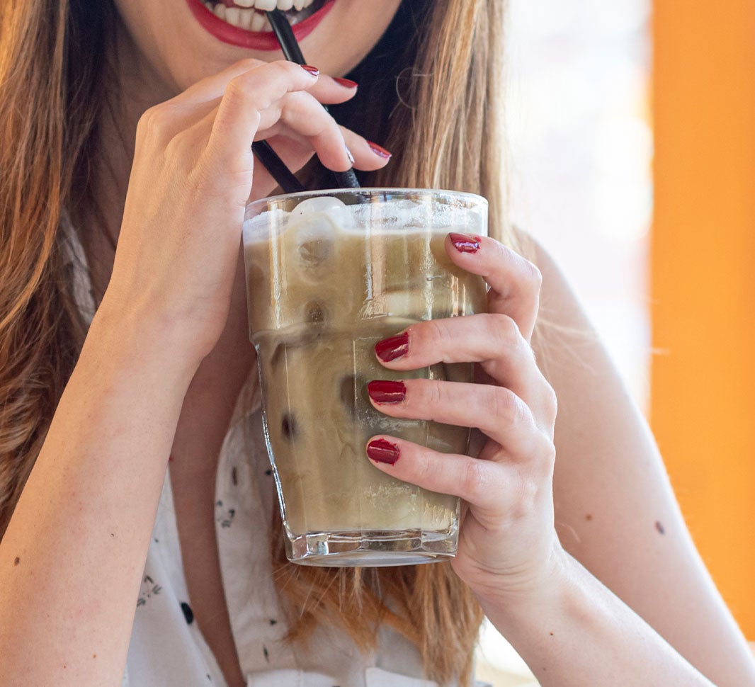 Person holding an iced cappuccino, sipping through a straw