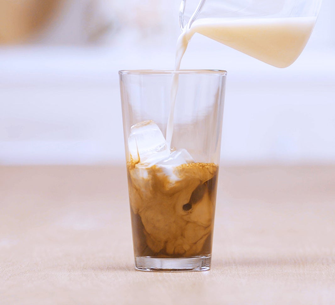 Pouring frothed milk over a glass of iced coffee