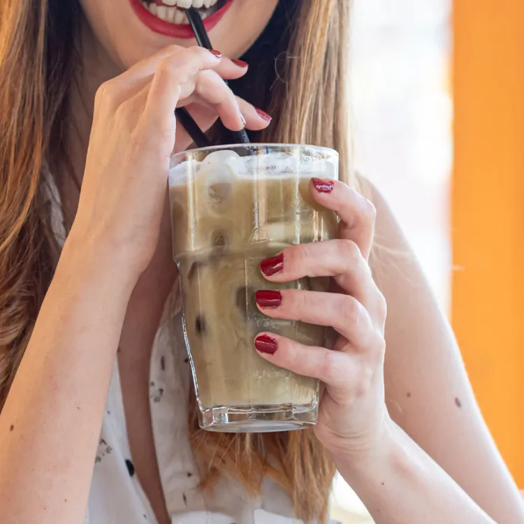 Person holding an iced cappuccino, sipping through a straw