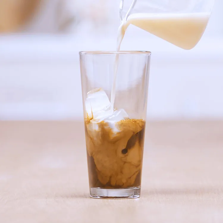Pouring frothed milk over a glass of iced coffee