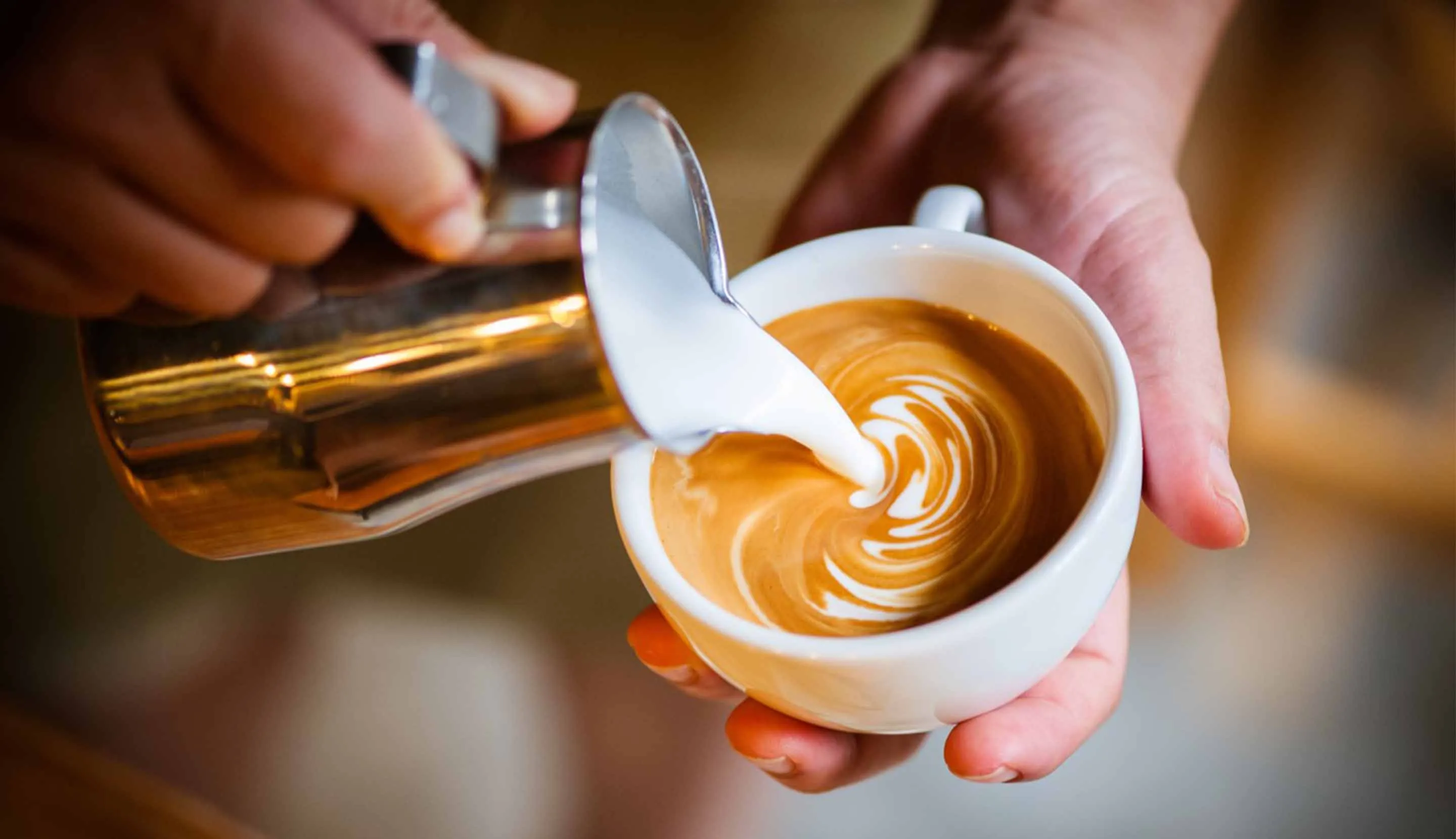 Adding frothed milk to make a cup of cappuccino coffee