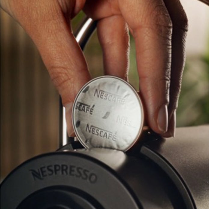 Een hand plaatst een NESCAFÉ® Roastery koffiecapsule in een Nespresso® koffiemachine.
