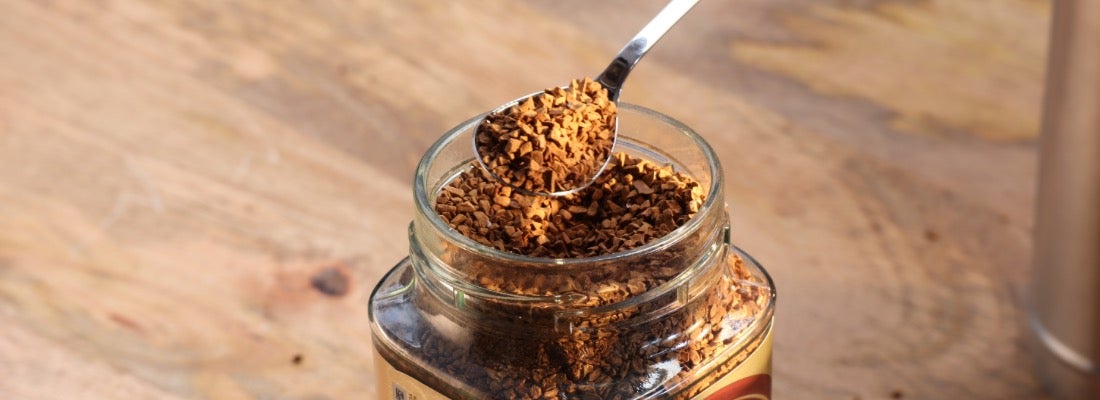 Oploskoffiekorrels op een lepel boven een glazen pot