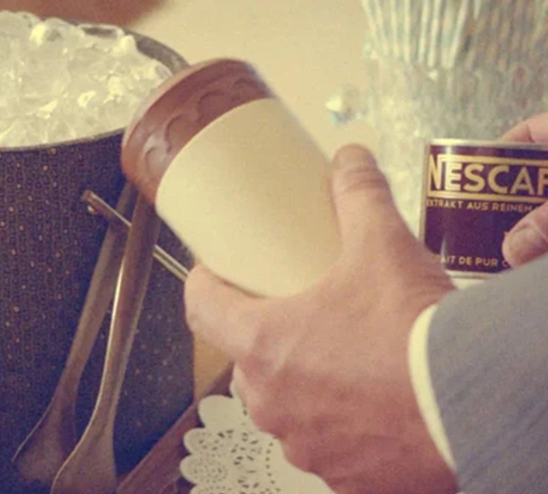 Човек държи чаша и кутия NESCAFÉ до купа с лед