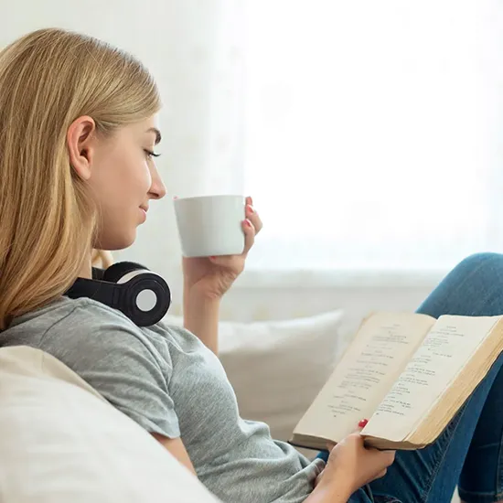 una niña bebiendo de una taza mientras lee un libro