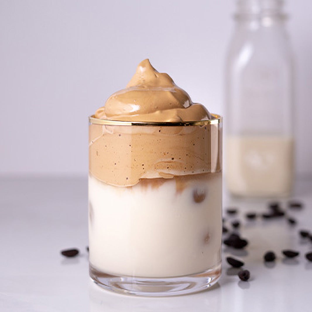 Un vaso de café dalgona recién preparado con una botella de leche atrás