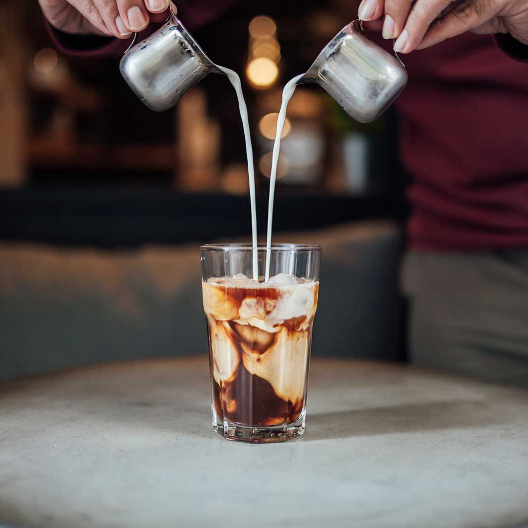 Una persona preparando un café bombón con dos tazas de leche condensada