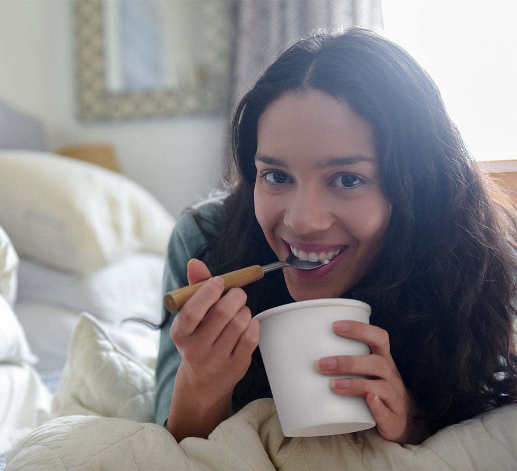 Mujer comiendo una taza de helado de café soluble en la cama 