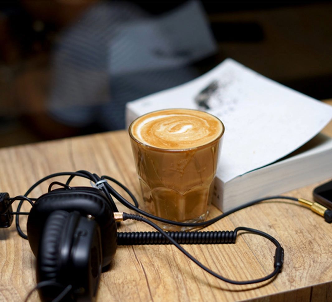 Audífonos, taza de café, celular y libro encima de una mesa