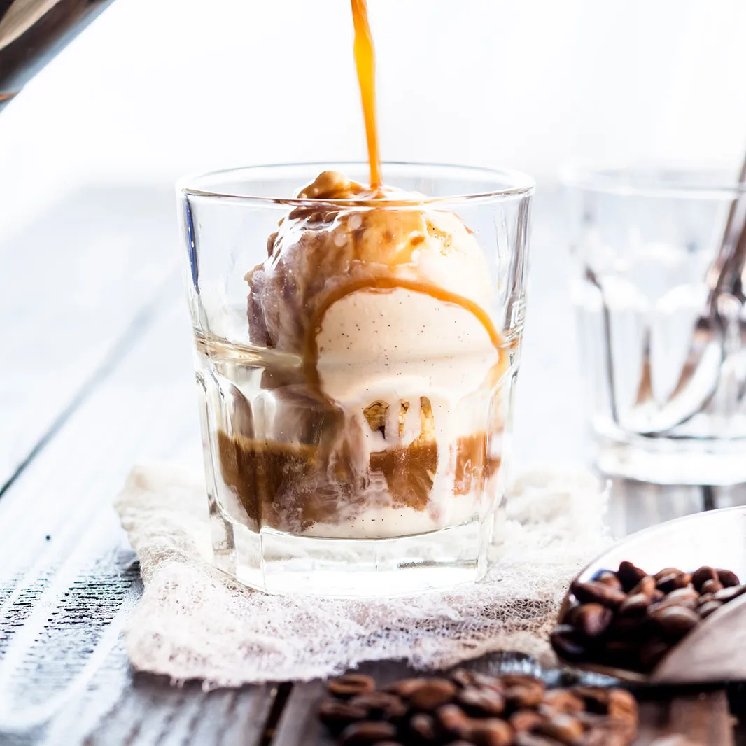 Café espresso vertido sobre una bola de helado para preparar un affogato