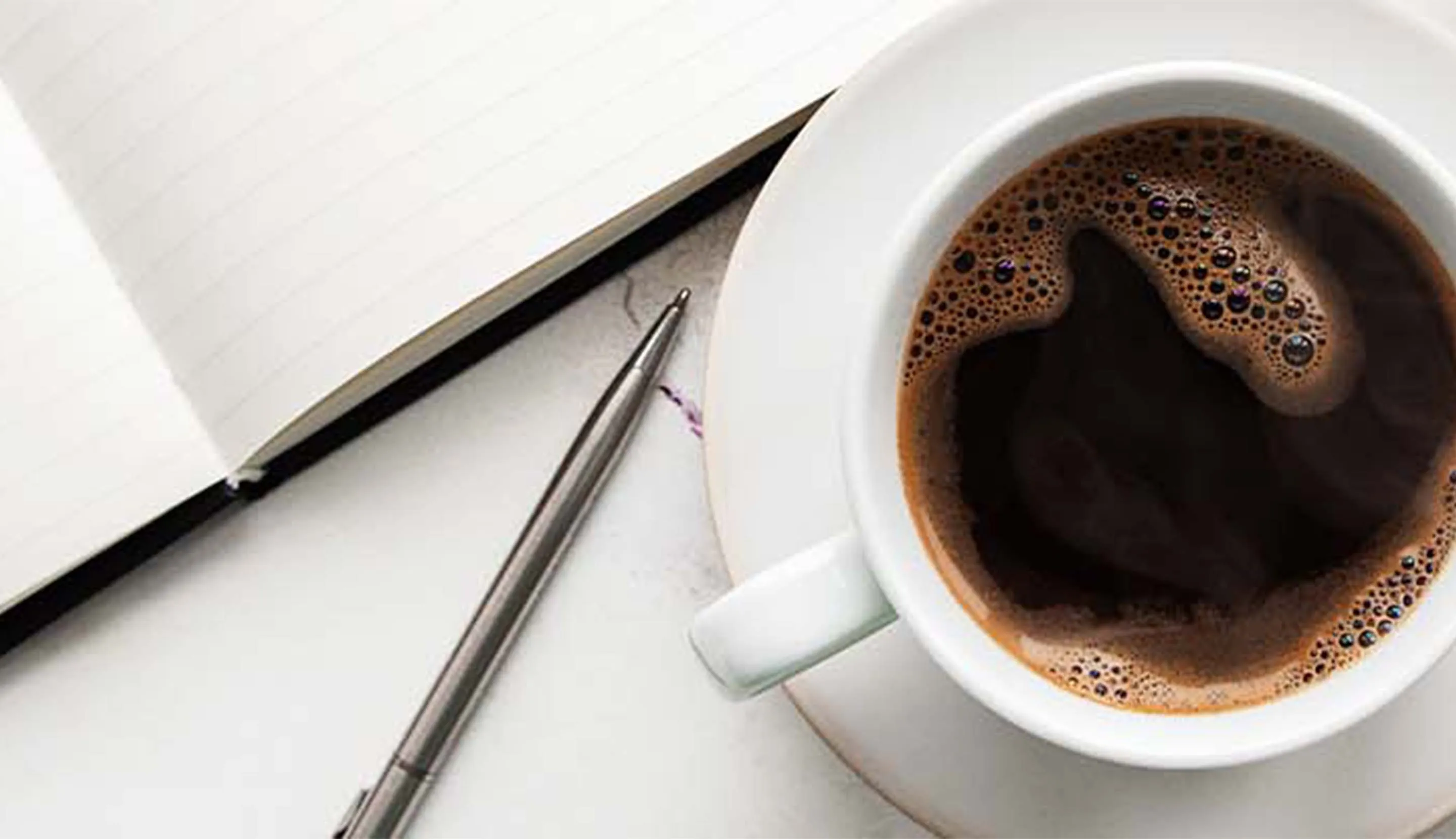 Taza de café expreso sobre una mesa rodeada de flores, libreta y gafas