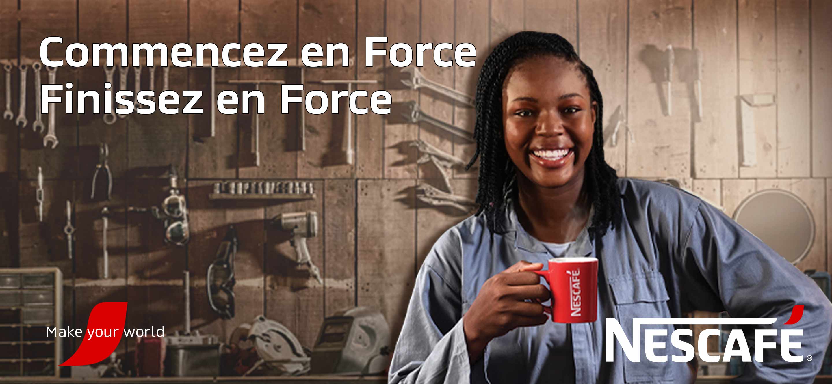 Une femme vêtue d'une combinaison bleue avec un grand sourire se tient devant un mur en bois avec plusieurs outils d'atelier tout en tenant une tasse NESCAFÉ rouge et un texte indiquant NESCAFÉ Commencez En Force, Finissez En Force