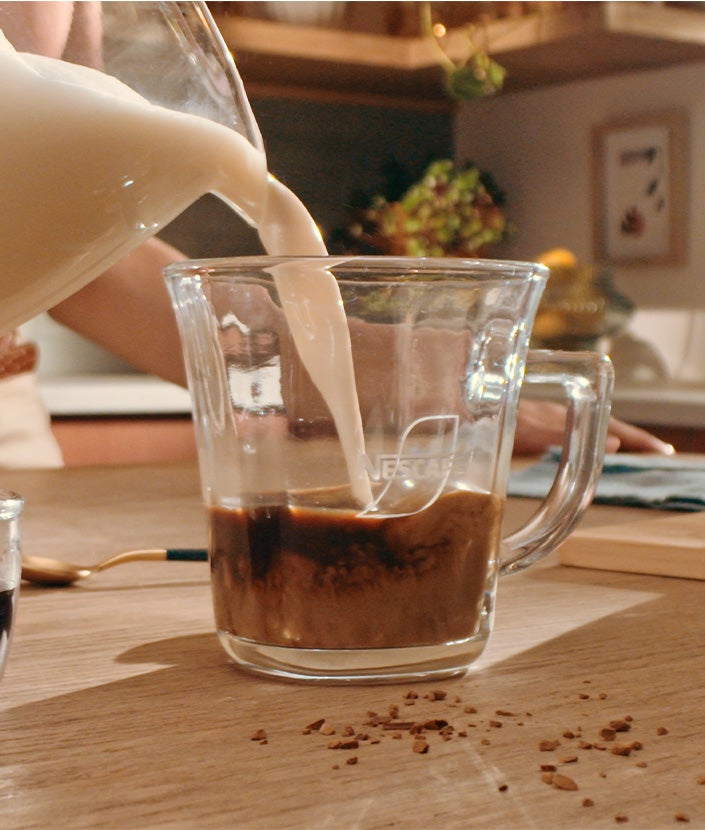 Milch wird in die Tasse mit Kaffee gegeben