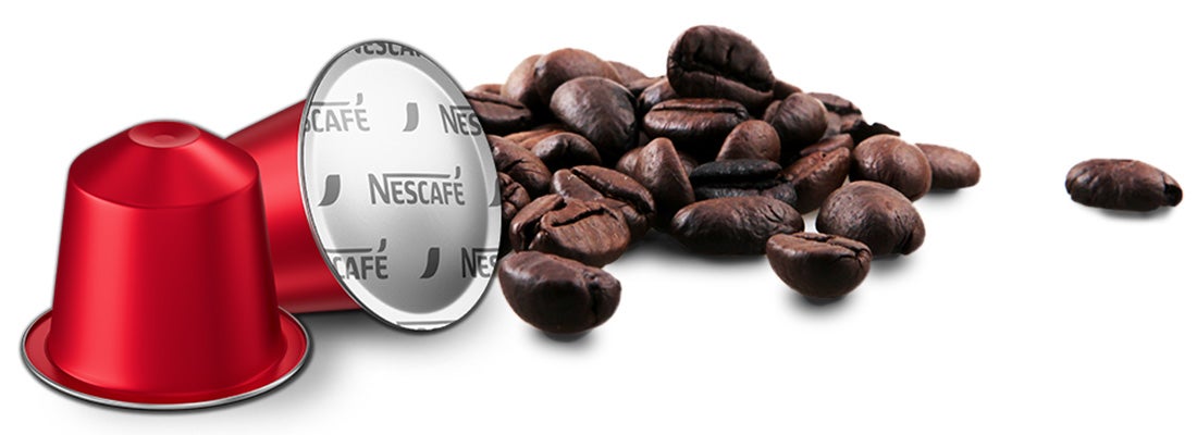 Cápsula de café NESCAFÉ® junto a granos de café tostados