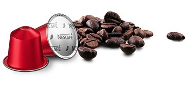 Cápsula de café NESCAFÉ® junto a granos de café tostados
