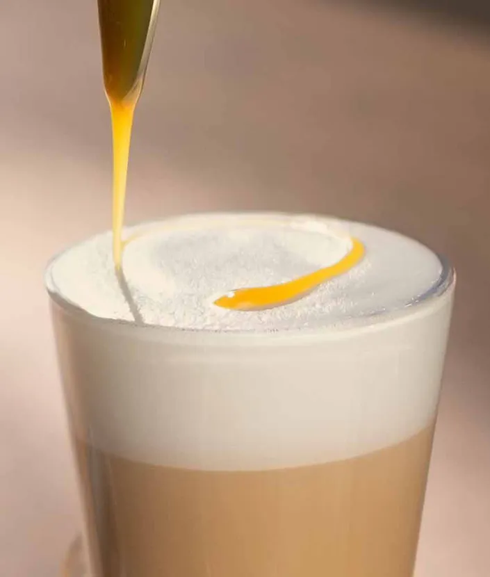 Une cuillère versant un filet de caramel sur le latte