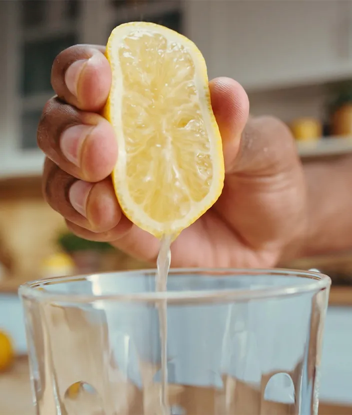 Une main pressant un demi-citron au-dessus d’un verre