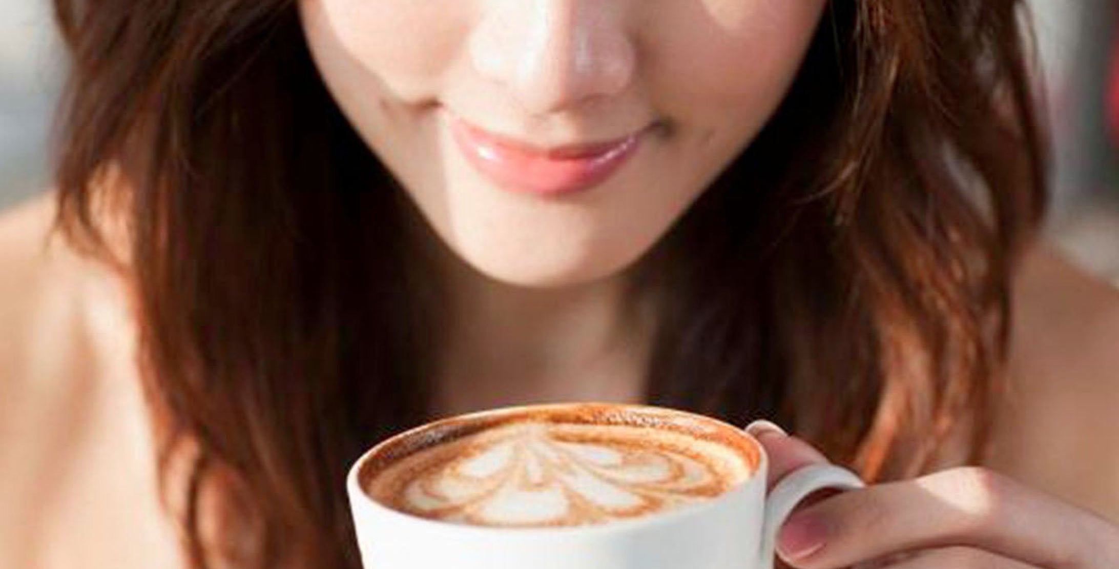 A lady smelling a cup of coffee