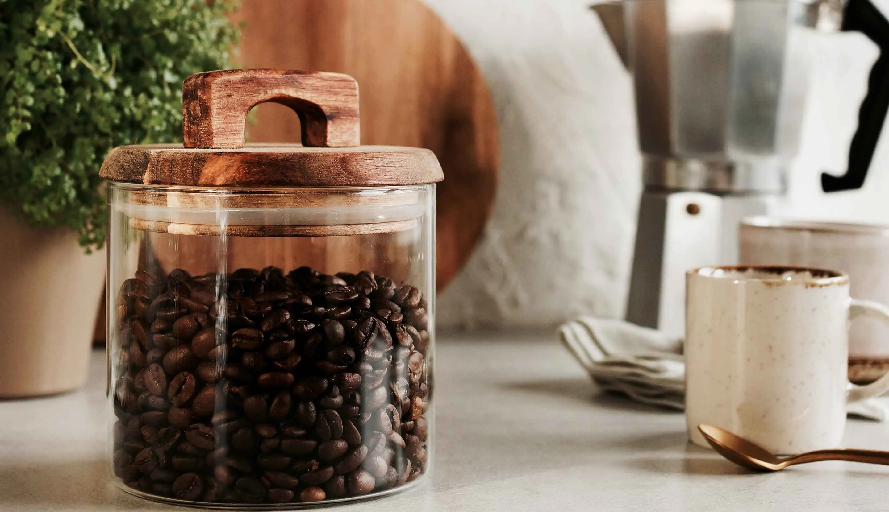 Jar of coffee beans on a kitchen counter next to a brewed coffee and coffee maker