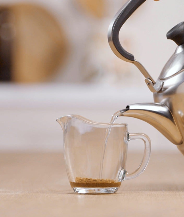 Ulijevanje NESCAFÉ Gold kave, žličice zaslađivača i vruće vode u šalicu