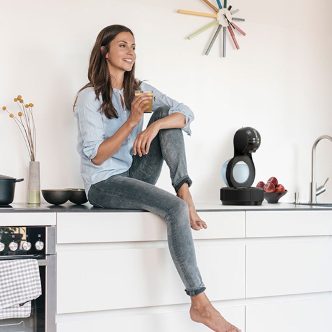 Žena sjedi na kuhinjskom elementu i pije NESCAFÉ Dolce Gusto Café Au Lait kavu