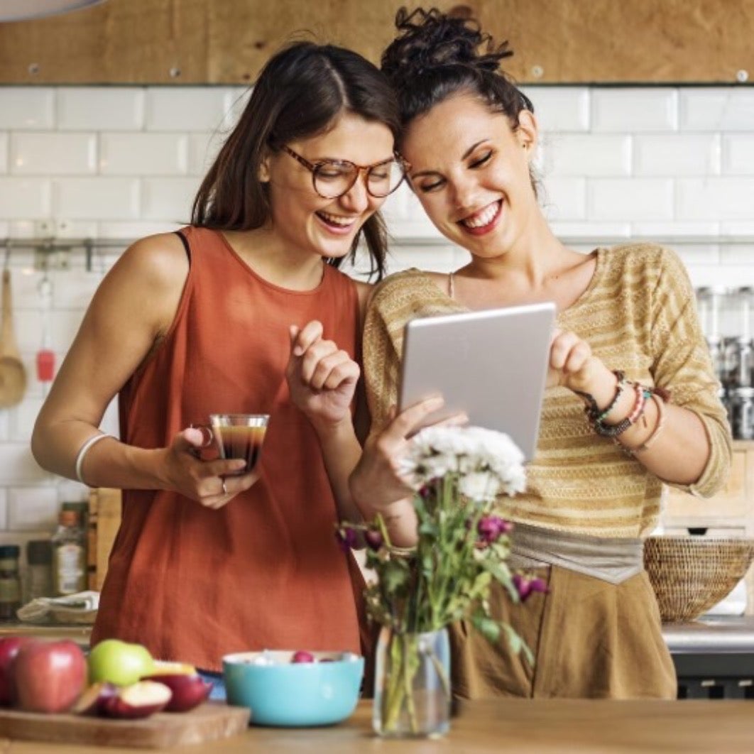 Dvije žene gledaju u tablet, a jedna od njih drži šalicu NESCAFÉ kave