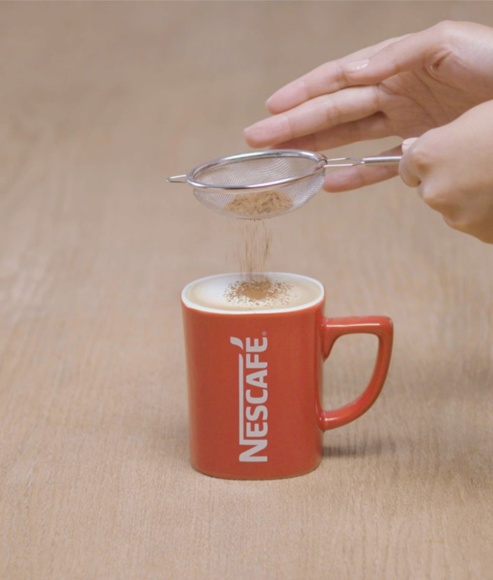 Ulijevanje pjenastog mlijeka u smjesu kave i sipanje kakaa u prahu