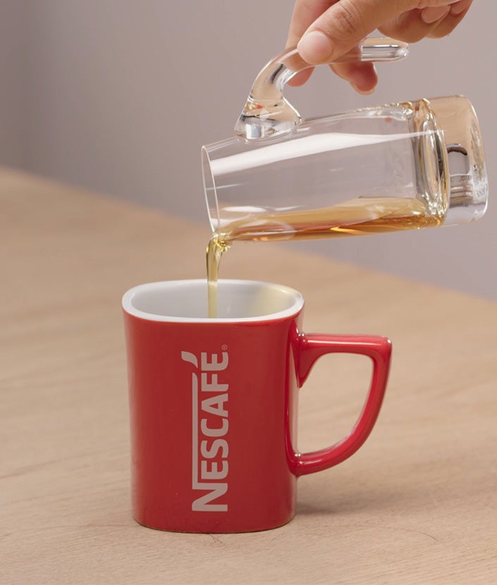 Dodavanje sirupa od lješnjaka u crvenu Nescafé šalicu