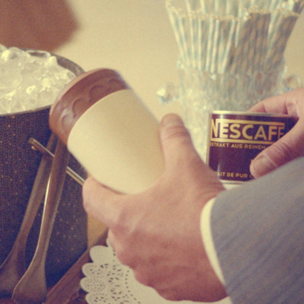 Osoba koja drži šalicu i NESCAFÉ proizvod pored kante s kockicama leda