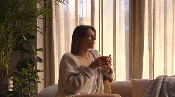 Žena sjedi na sofi držeći u ruci šalicu NESCAFÉ Crema kave