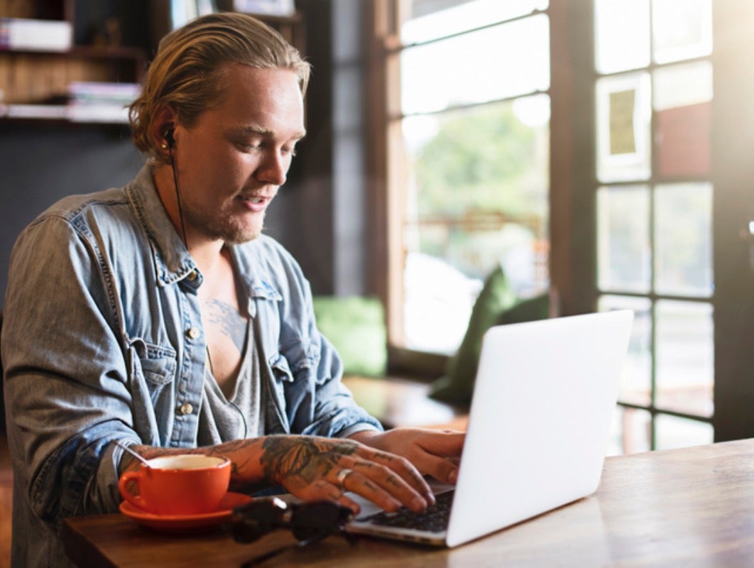 Muškarac sjedi uz šalicu kave i radi na laptopu