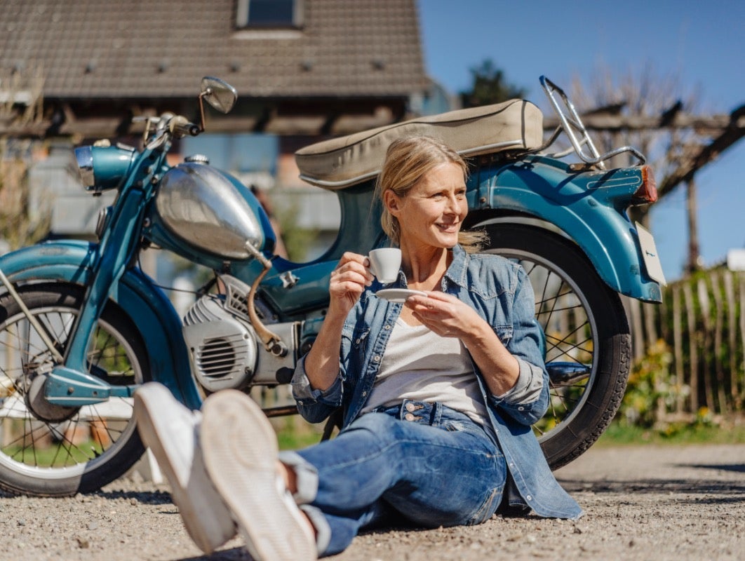 Žena sa šalicom kave sjedi uz motor