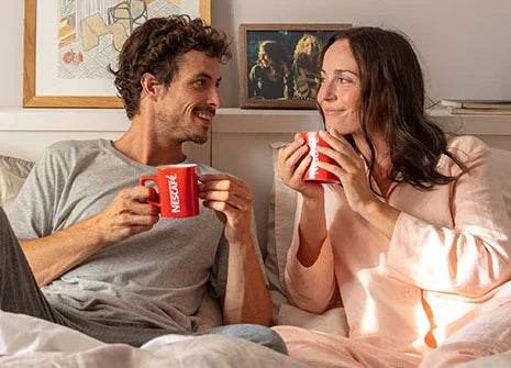 Para delektuje się NESCAFÉ Classic w łóżku, uśmiechając się do siebie.