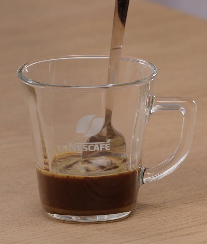 Mešanje kafe i vode u čaši kašikom