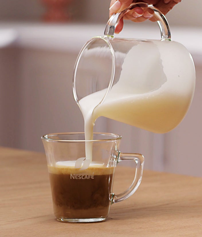 Sipanje penušavog mleka u šolju sa mešavinom kafe