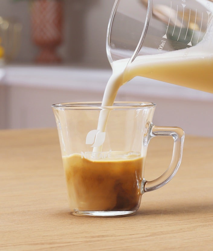 Sipanje penušavog mleka u šolju sa mešavinom kafe