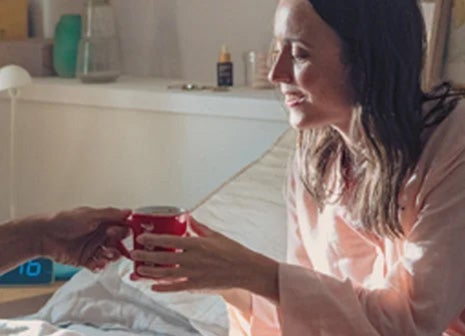 Žena grabi NESCAFÉ šolju i sprema se da uživa u kafi u krevetu.