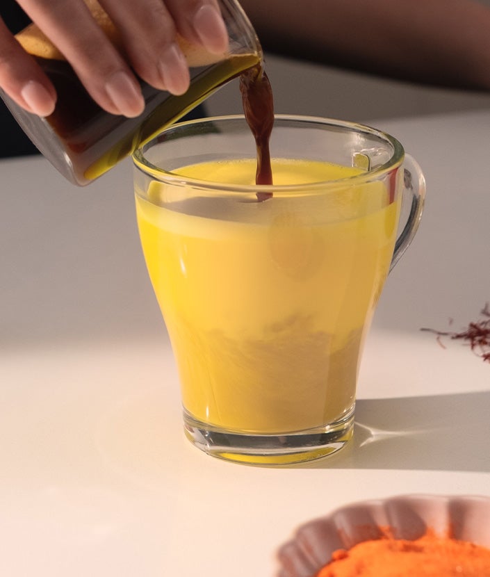 Hand pouring melted brown sugar into saffron latte