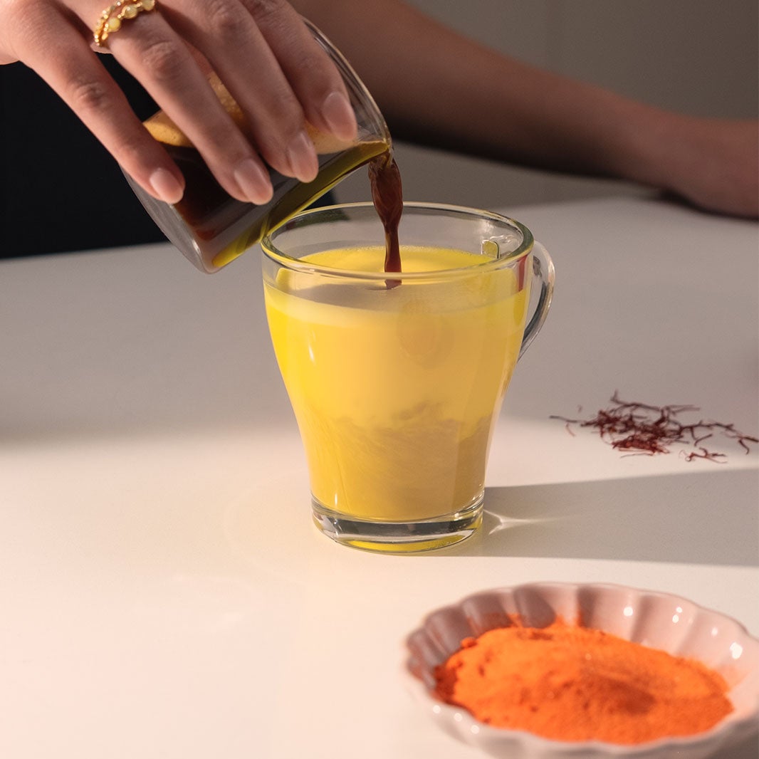Hand pouring melted brown sugar into saffron latte
