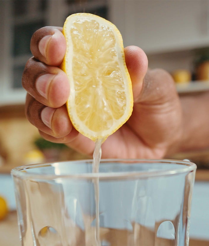 Hand squeezing half a lemon into a glass