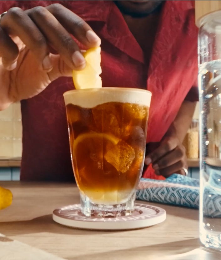 Hand adding a lemon slide to a glass of mazagran iced coffee