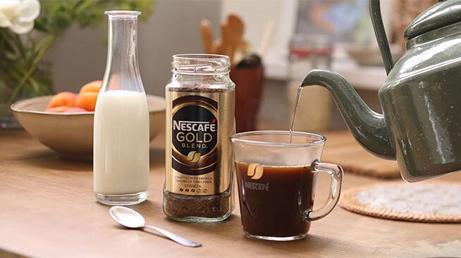 Kettle pouring water into mug next to jar of coffee and milk