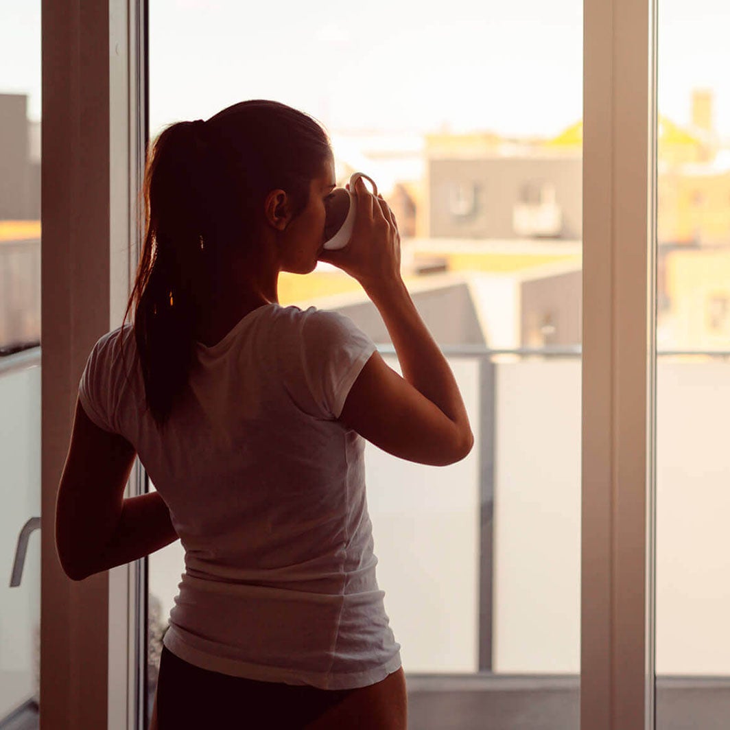 žena pije kávu ráno pri okne