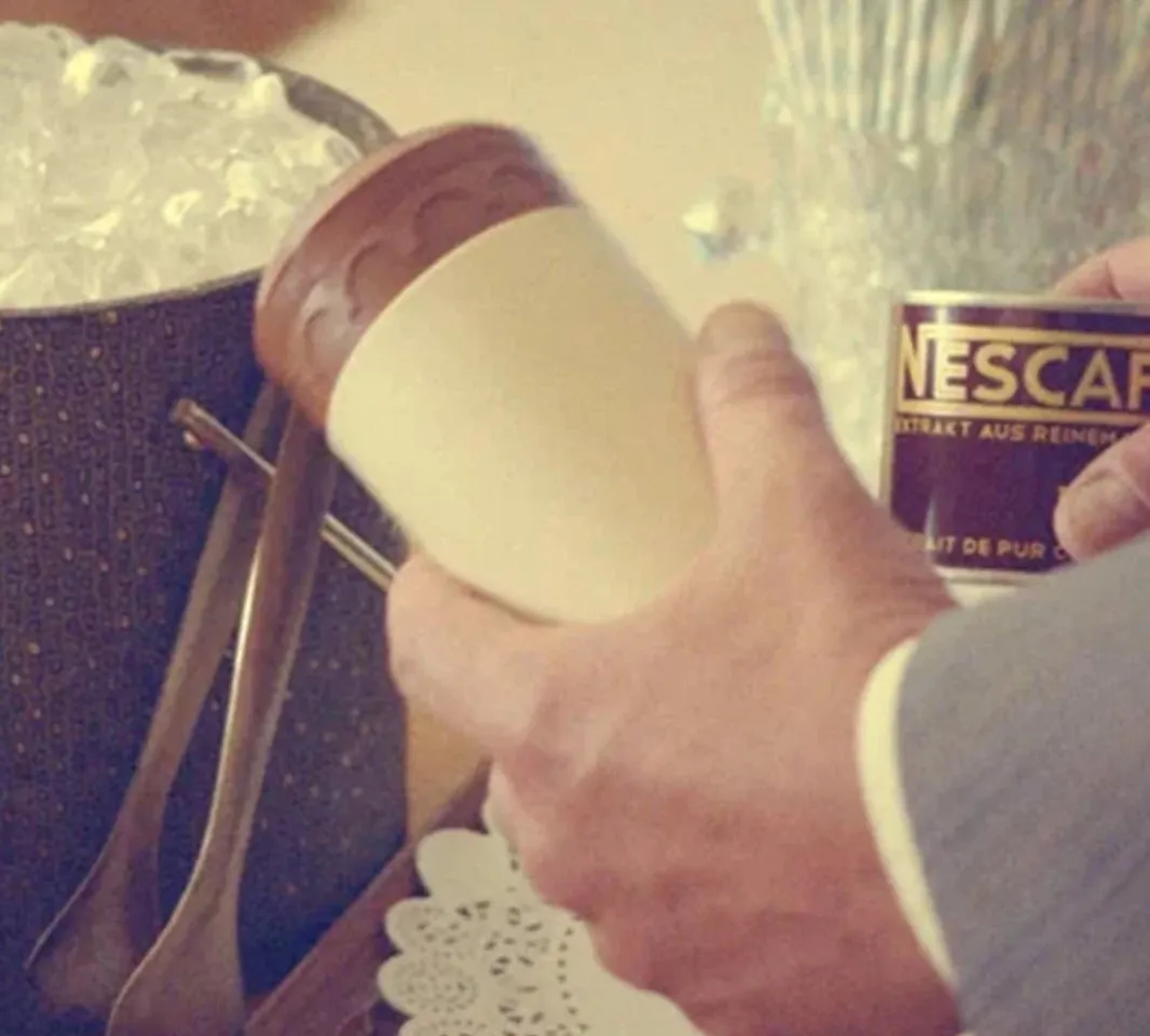 Людина тримає чашку та продукт NESCAFÉ біля відра з кубиками льоду