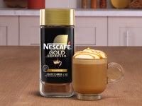 NESCAFÉ® Gold Blonde Espresso packaging next to a caramel latte on a wood surface.