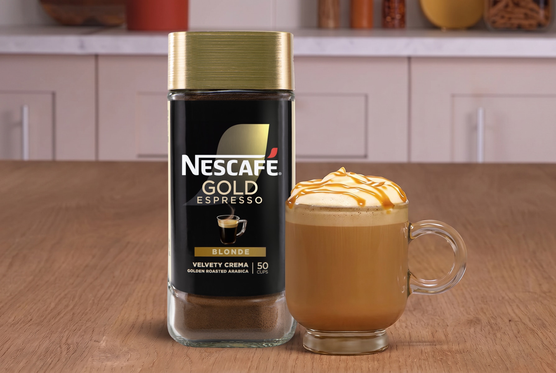 NESCAFÉ® Gold Blonde Espresso packaging next to a caramel latte on a wood surface.
