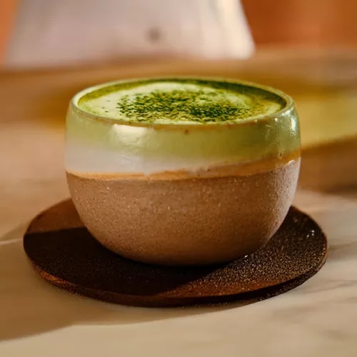 Photo: ceramic cup of frothy matcha latte with green powder, on a saucer