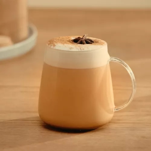 Photograph: glass mug with frothy spiced latte topped with star anise on wood